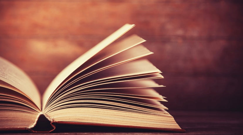 An open book with its pages fanned out, resting on a wooden surface against a warm, softly blurred background.