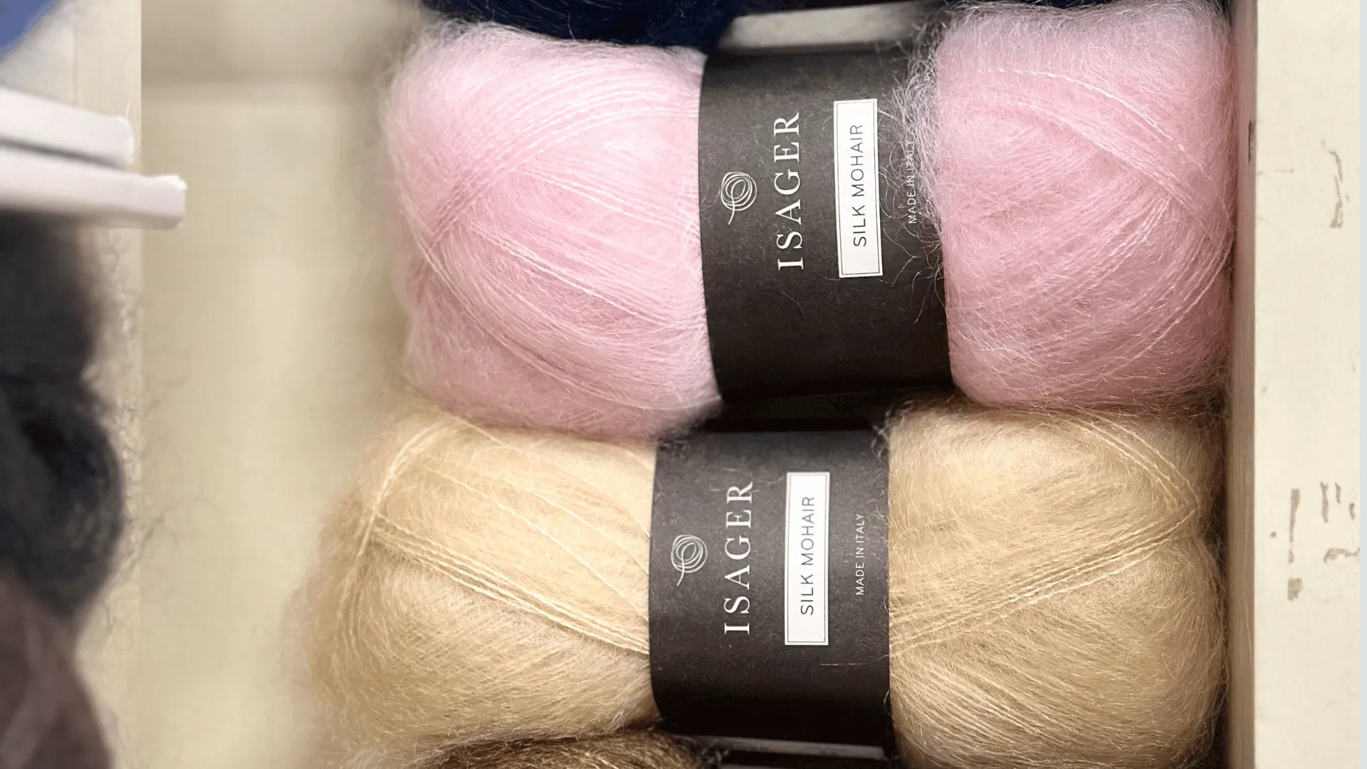 Two skeins of Isager Silk Mohair yarn, one pink and one beige, are displayed side by side in a drawer. Both skeins have black labels with the brand name and yarn type.