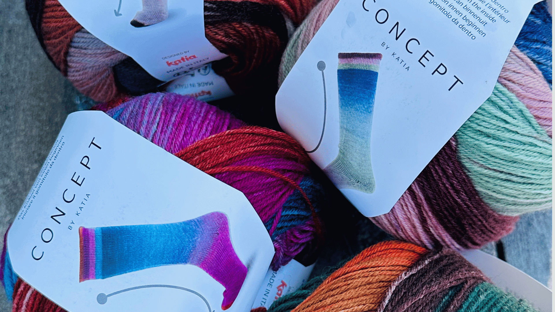 Several skeins of colorful yarn from the Katia Concept brand are shown, with labels featuring images of knitted socks in gradient rainbow shades.
