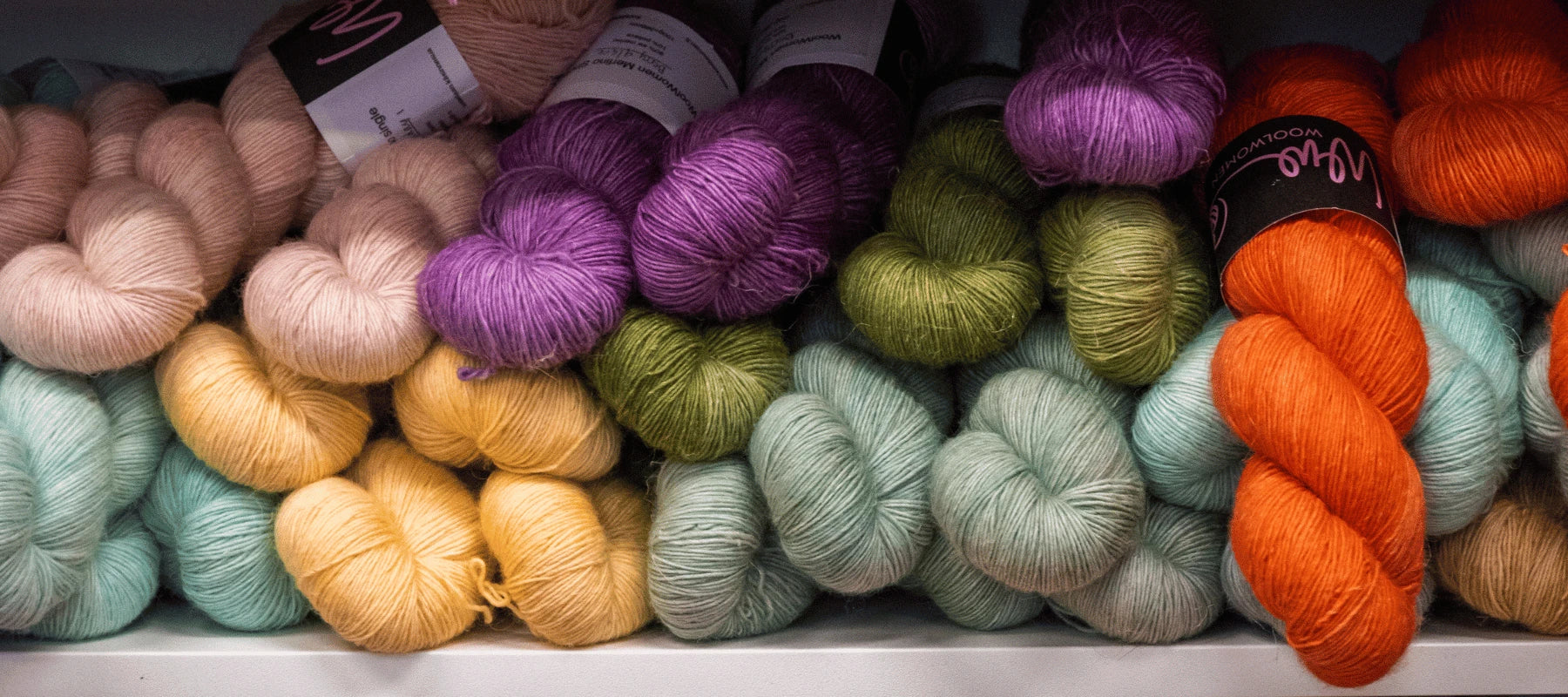 Skeins of yarn in various colors—peach, purple, green, orange, and light blue—are neatly stacked on shelves.