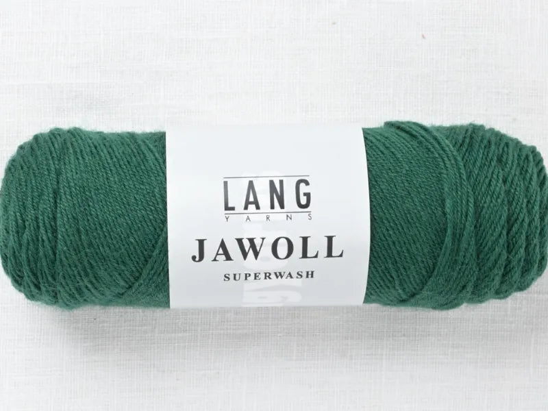 A skein of green yarn, Timo sukka ohje fingerin ja Lang jawoll, rests on a white textured surface—ideal for your next neulontaohje or sock knitting project.