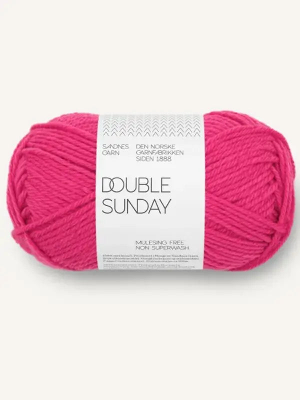 A skein of bright pink Sandnes Garn Double Sunday merino wool yarn wrapped with a white paper label.