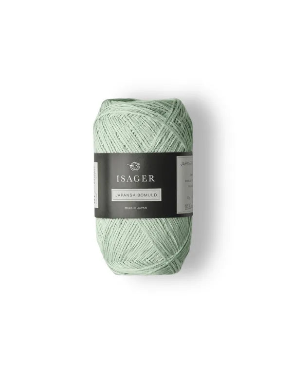 A skein of pale green Isager Japansk Bomuld puuvillalanka with a black and gray label, ideal for fresh kesäneuleet, displayed on a plain white background.