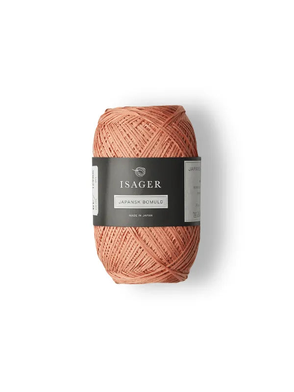 A peach-colored ball of Isager Japansk Bomuld cotton yarn with a black label, set against a white background. The smooth, neatly wound yarn is ideal for lightweight summer knits.