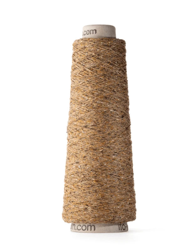 A tall spool of coarse, brown jute twine stands upright on a cardboard cone against a white background, contrasting with the smooth texture of Ito Kinu silk yarn commonly used in summer knits.