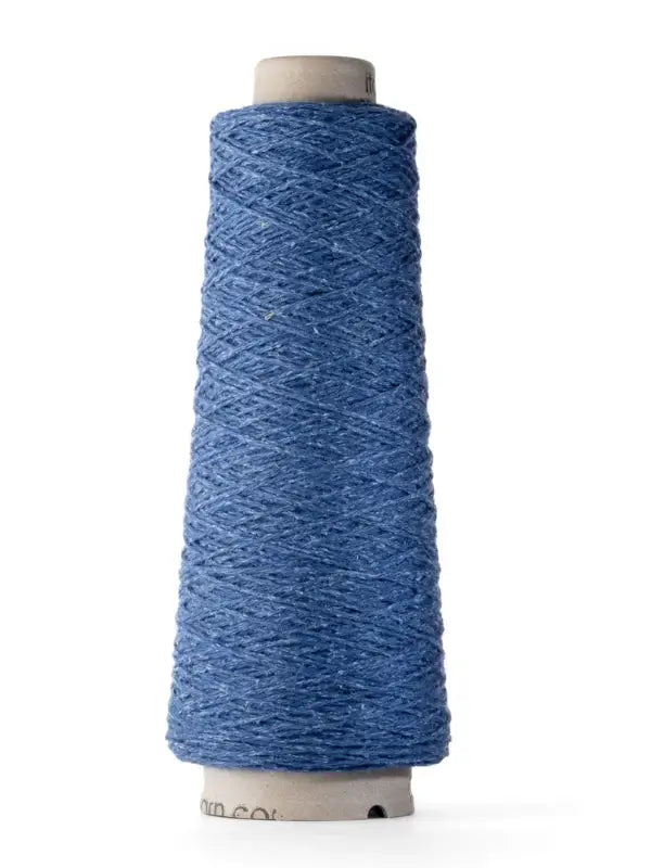 A spool of Ito Yarn Shimo in a blue shade, crafted from luxurious merinovillalanka, stands upright against a white background with the thread tightly wound around its cone-shaped cardboard core.