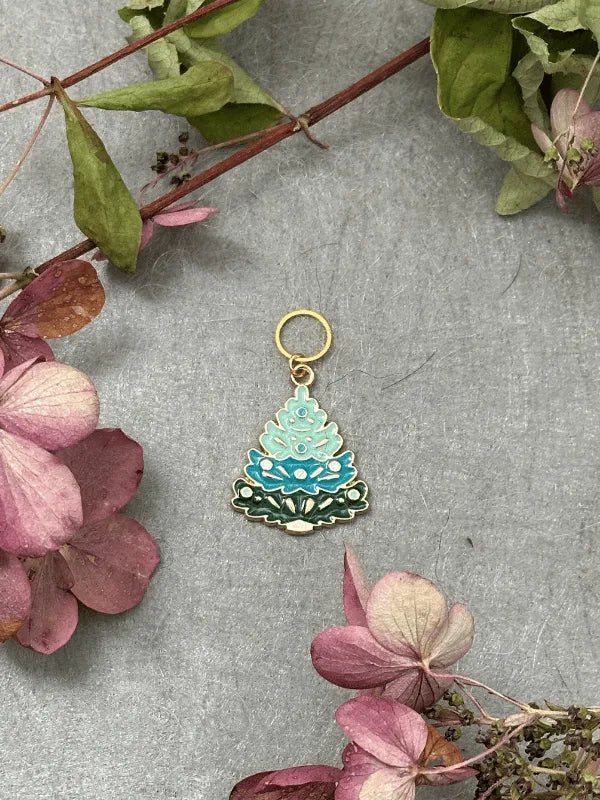 The KNITS by cindy ekman silmukkamerkit is a decorative enamel keychain in layered blue and green tree shapes, displayed on gray with dried flowers—an ideal gift for neulonta fans seeking kauniit silmukkamerkit.