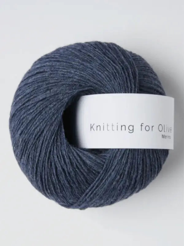 A ball of dark blue Knitting for Olive Merino yarn, Öko-Tex certified and neatly wound with a white label, rests on a light surface.