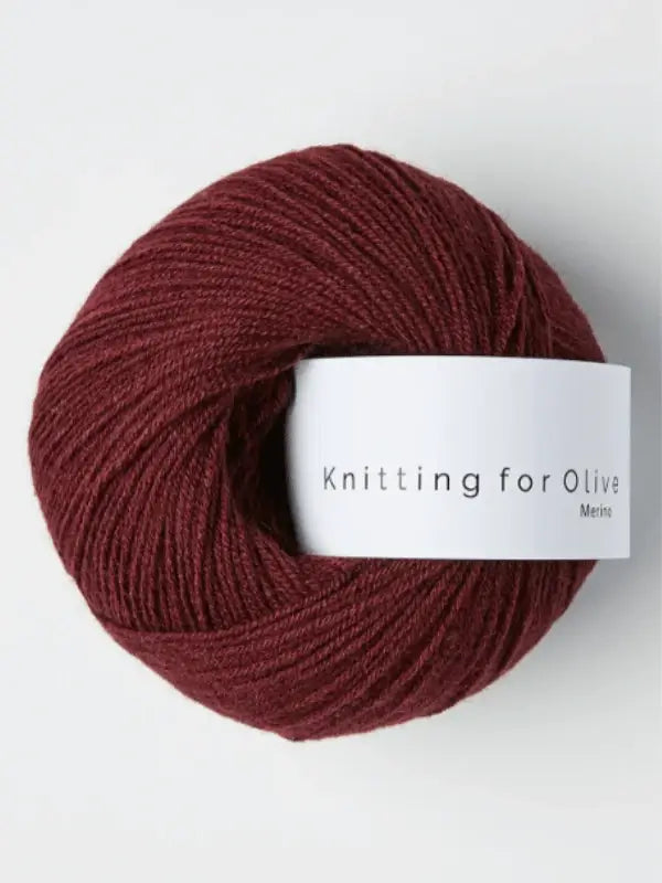 A ball of deep burgundy Knitting for Olive Merino wool yarn with a white label, displayed on a plain light background.