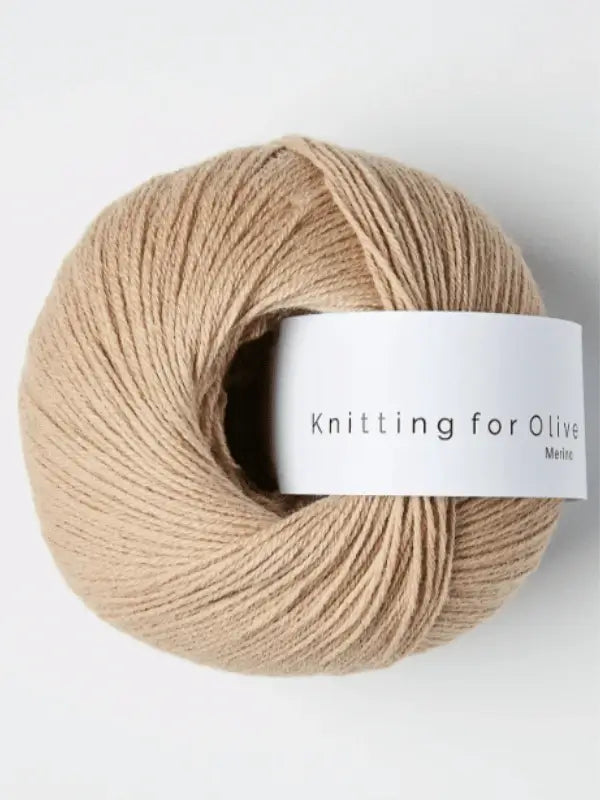 A beige ball of Knitting for Olive Merino yarn with a white label rests on a plain, light background.