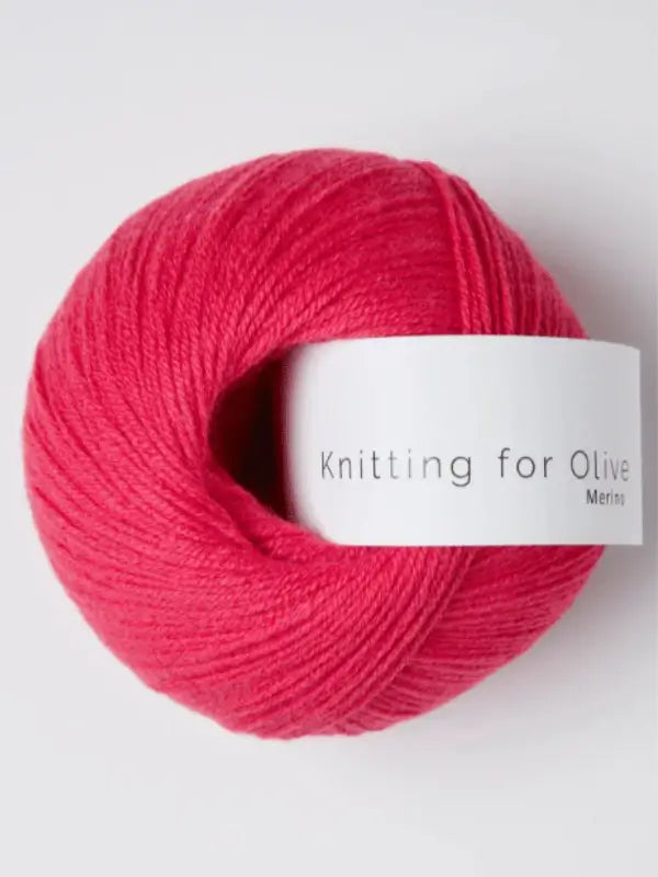 A skein of bright pink Knitting for Olive Merino yarn with a white label rests on a plain light background, highlighting its softness and Öko-Tex certified quality.