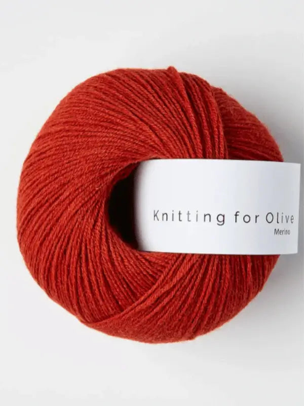 A ball of deep red Knitting for Olive Merino yarn with a white label rests on a plain white background. This yarn is Öko-Tex certified, ensuring high standards of quality and safety.