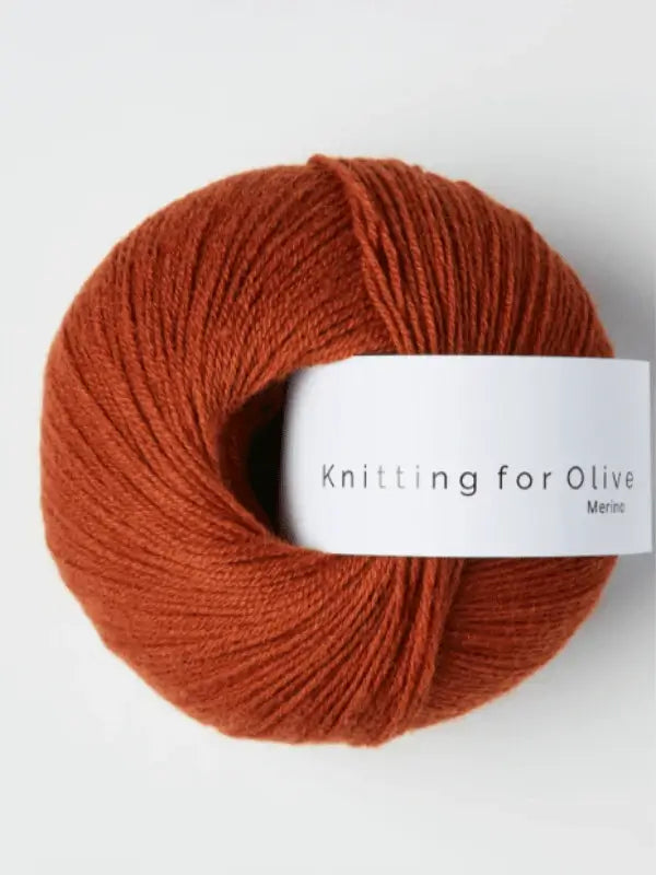 A ball of reddish-brown Knitting for Olive Merino yarn with a white label sits against a plain, light background.