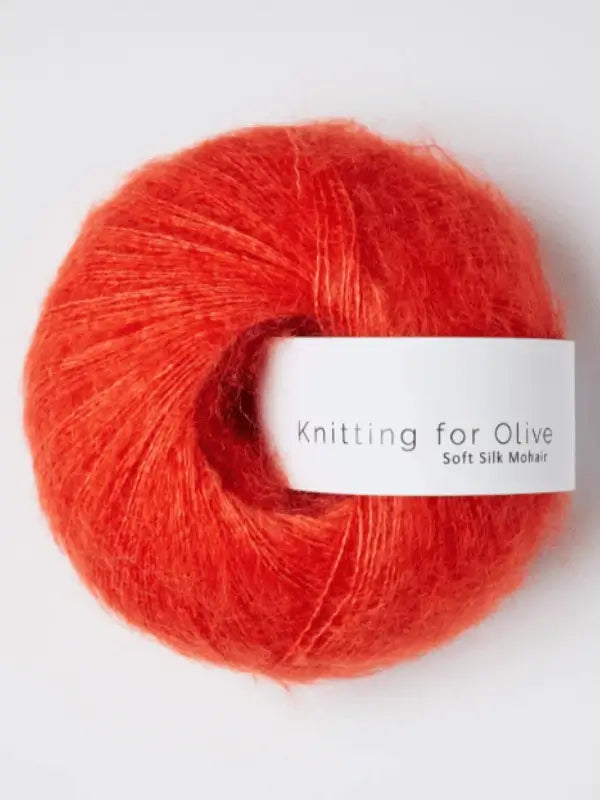 A skein of vivid orange Knitting for Olive Soft Silk Mohair yarn, made from vastuullinen mohair and premium kid mohair lanka, rests on a white surface.