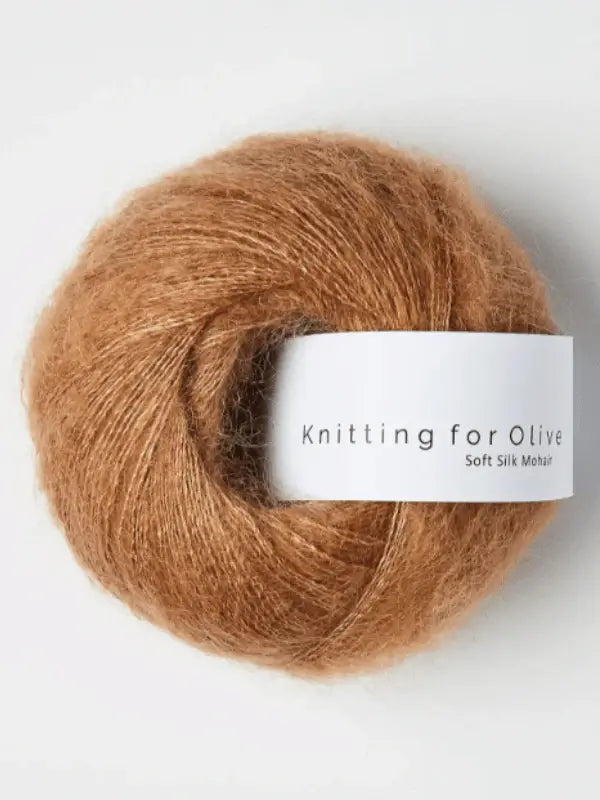 A ball of light brown mohair yarn labeled "Knitting for Olive Soft Silk Mohair" rests on a plain background. This sustainable mohair blend combines kid mohair and silk for an exceptionally soft, eco-friendly knitting experience.