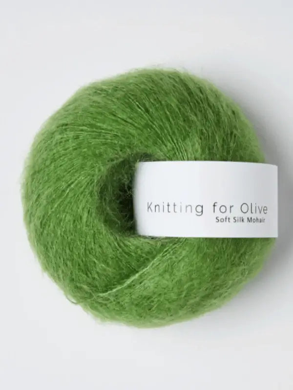 A ball of vivid green Knitting for Olive Soft Silk Mohair yarn, crafted from a sumptuous blend of kid mohair and silk, with a white label bearing the product name displayed against a light background. This yarn is made in accordance with the Responsible Mohair Standard, guaranteeing both high quality and ethical sourcing.