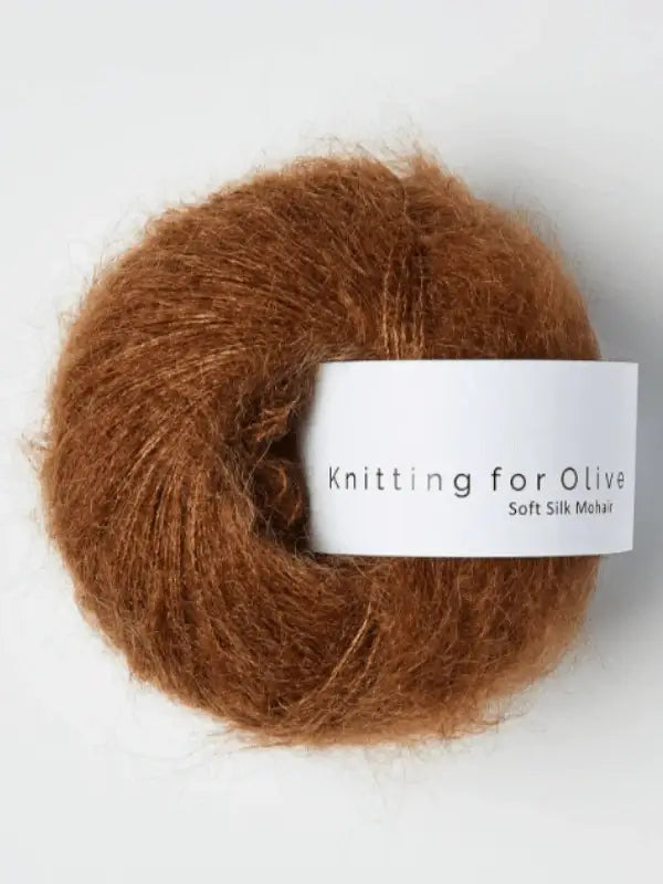 A ball of Knitting for Olive Soft Silk Mohair yarn—fluffy and brown—made from mohair and silk, rests on a white background.