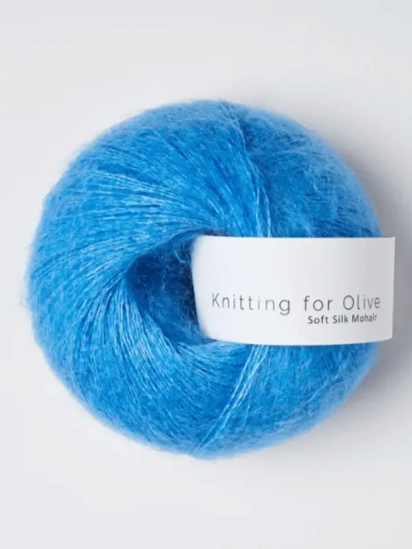 A ball of vibrant blue Knitting for Olive Soft Silk Mohair yarn with a white label displaying the product name, set against a neutral background and made from fibers certified by the Responsible Mohair Standard.