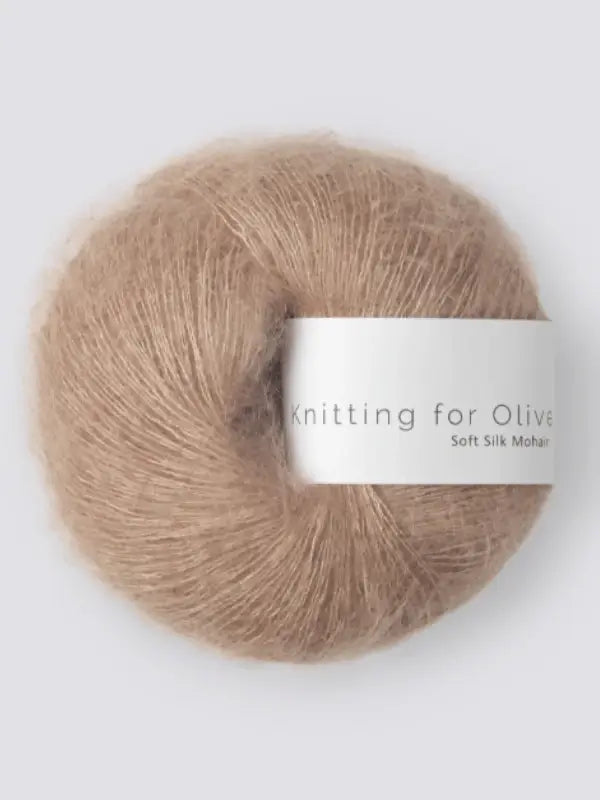 A ball of light brown Knitting for Olive Soft Silk Mohair yarn, featuring a white label with the product name, made from vastuullinen mohair and kid mohair lanka, is displayed against a plain light background.