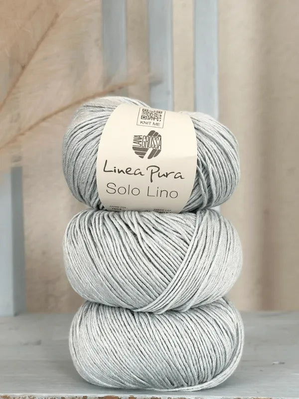 Three light gray balls of Lana Grossa Solo Lino yarn are stacked vertically, the top one showing its label. This vegan yarn is neatly wound and displayed against a neutral background.