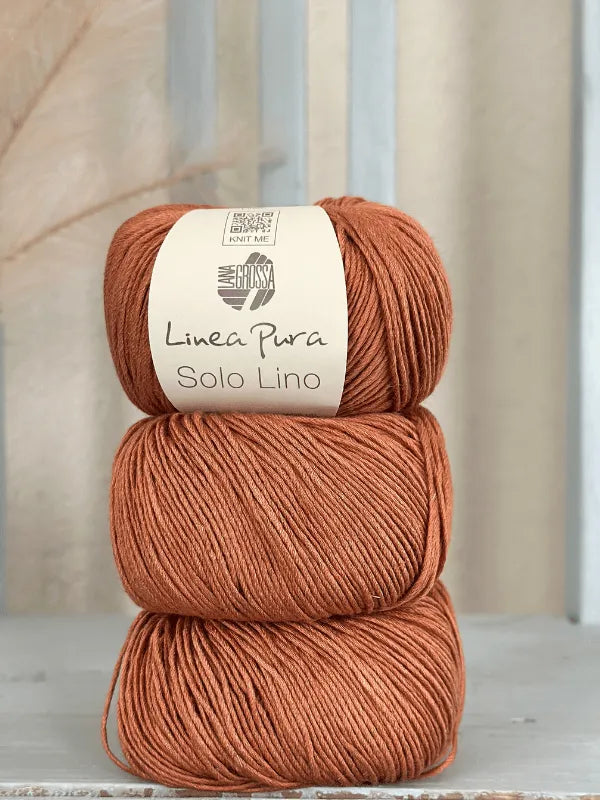 Three stacked balls of rust-colored Lana Grossa Solo Lino, a vegan linen yarn, with the top ball showing the Solo Lino label, set against a softly blurred neutral background.
