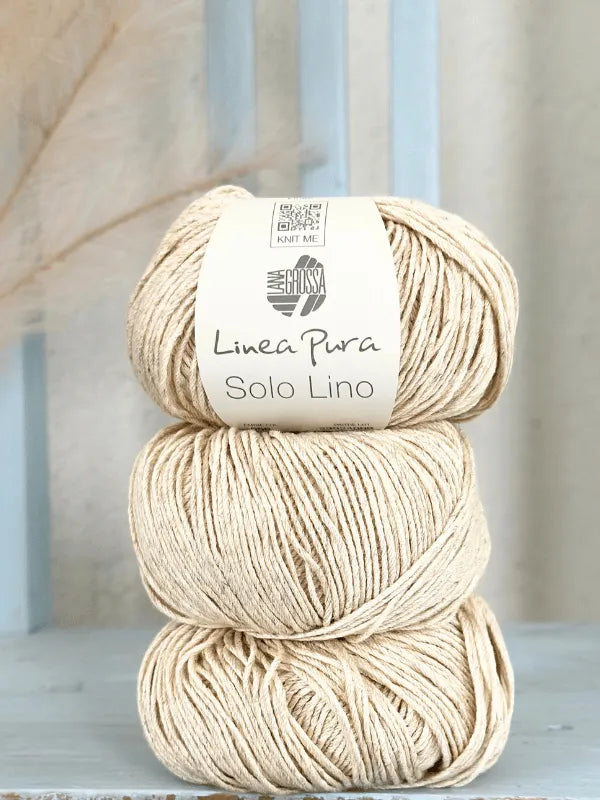 Three beige balls of Lana Grossa Solo Lino, a vegan yarn, are stacked vertically. The label on the top ball shows the product name and brand. The background features soft blue and neutral tones.