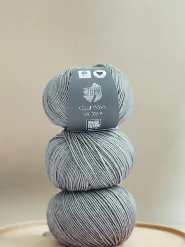 Three balls of light grey Lana Grossa Cool wool vintage merino wool yarn stacked vertically, with a label on the top ball reading 1990s.