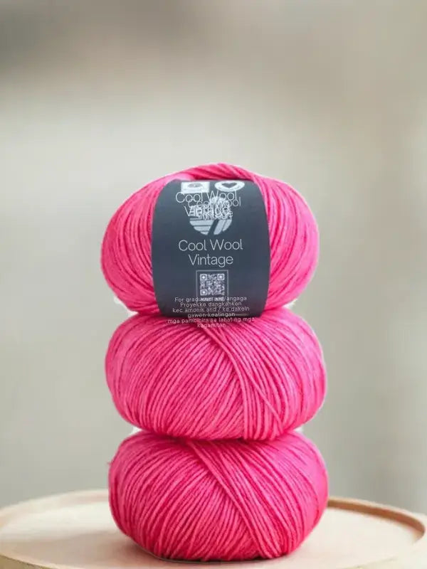 Three stacked balls of bright pink Lana Grossa Cool wool vintage merinovillalanka with a central product label.