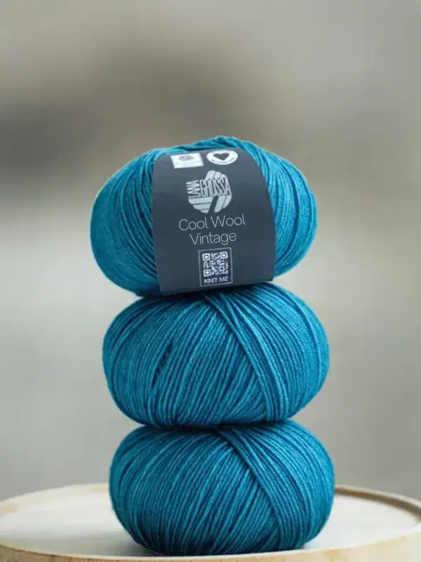 Three stacked balls of teal Lana Grossa Cool wool vintage yarn, with a product label on the top ball.