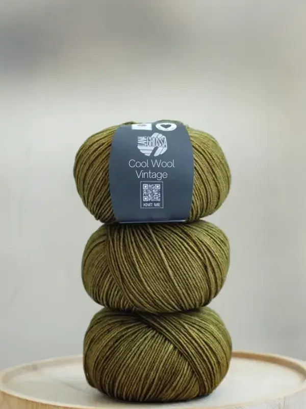 A stack of three olive green skeins of Lana Grossa Cool wool vintage merino wool yarn.