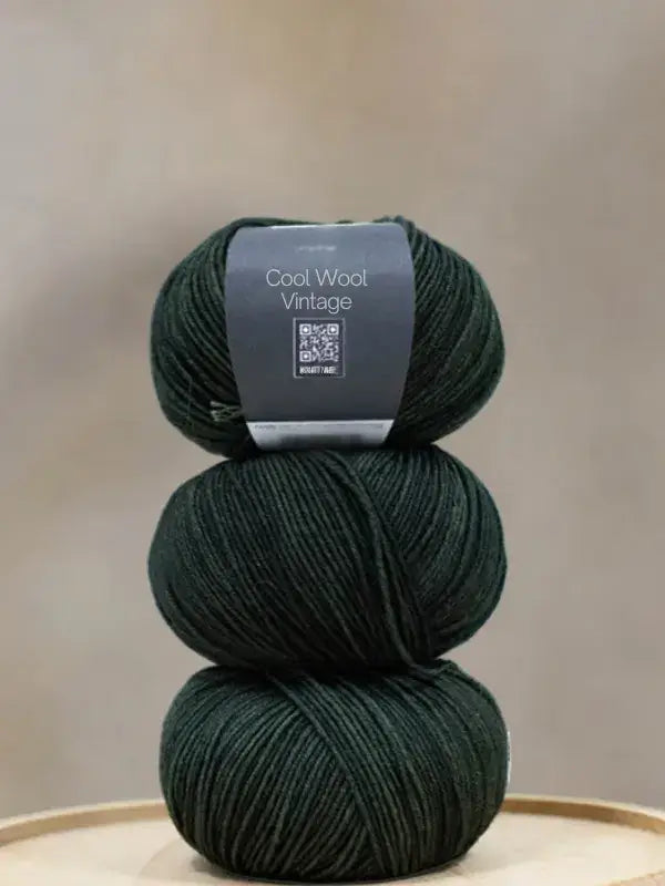 A stack of three balls of dark green Lana Grossa Cool wool vintage yarn with a product label on the top ball.