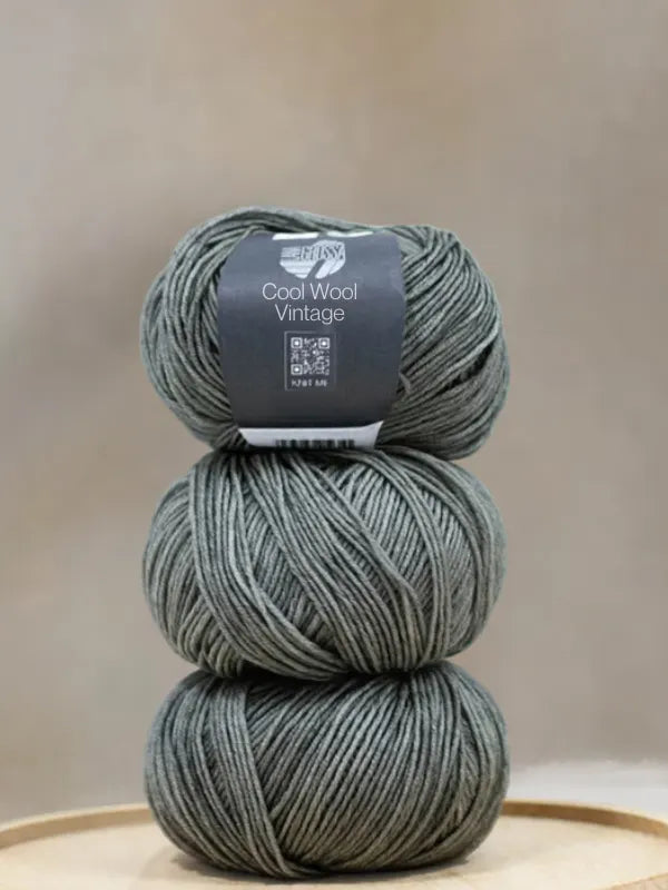 Three skeins of sage green Lana Grossa Cool wool vintage yarn stacked vertically with a label on the top skein.
