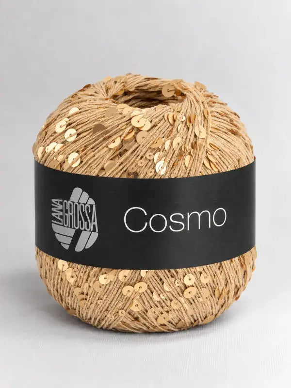 A ball of light brown Lana Grossa Cosmo yarn embellished with gold sequins and wrapped in a black paper label.