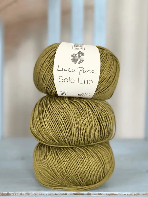Three olive-green Lana Grossa Solo Lino balls stacked, label on the top one. This vegan yarn rests on a light blue wooden surface—ideal for eco-friendly, stylish knitting projects.
