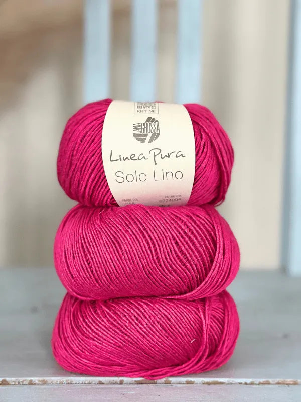 Three skeins of bright pink Lana Grossa Solo Lino yarn are stacked on a wooden surface. The top skein’s label shows the eco-friendly, vegan yarn, made with soft fibers.