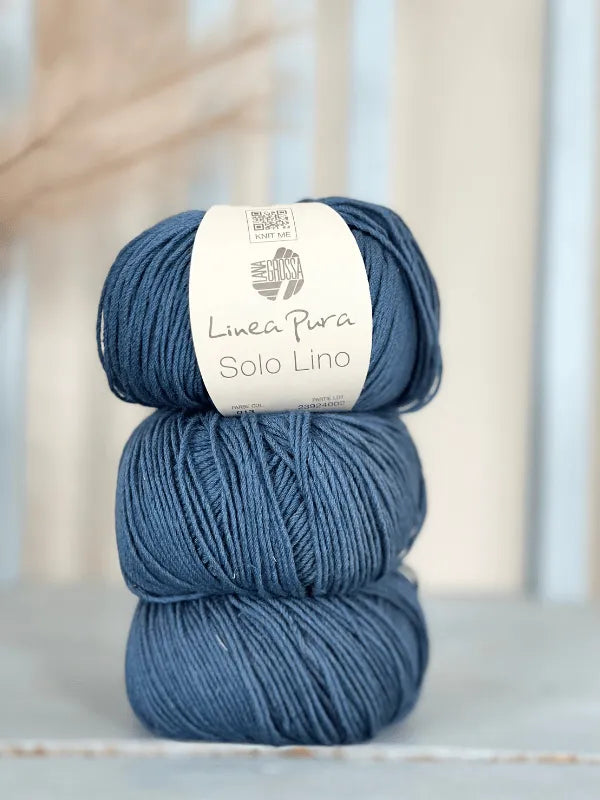 Two skeins of dark blue Lana Grossa Solo Lino yarn are stacked with white labels. A softly blurred neutral background highlights this beautiful vegan yarn.
