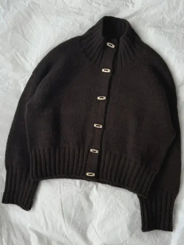 A dark brown, long-sleeved Hannah Jacket knit cardigan with a high collar and white buttons, featured in the PetiteKnit Hannah Jacket neuleohje -Suomi.