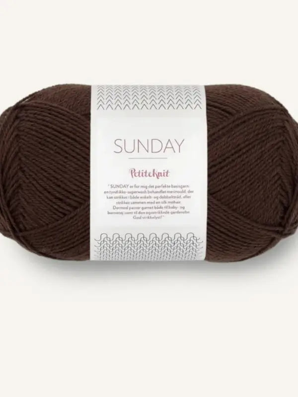 A skein of dark brown, fingering-weight yarn labeled Sandnes Garn Sunday with decorative text and patterns on a white paper band around the middle. This soft merino wool yarn is mulesing-free, ensuring both quality and ethical sourcing.