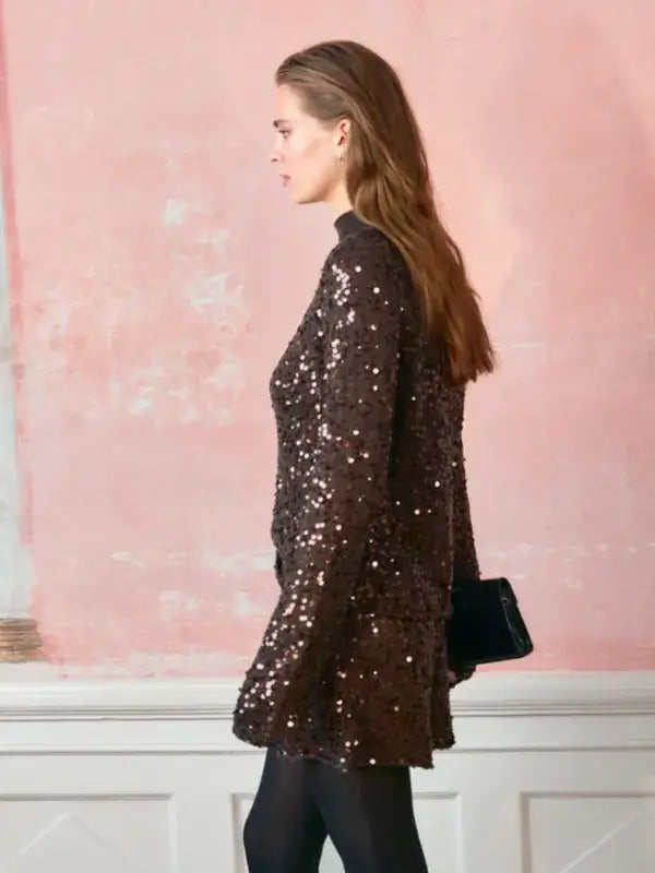 A woman wearing a dark brown, long-sleeved Sandnes Garn Isla Sweater – neulesetti Paljett covered in sequins.