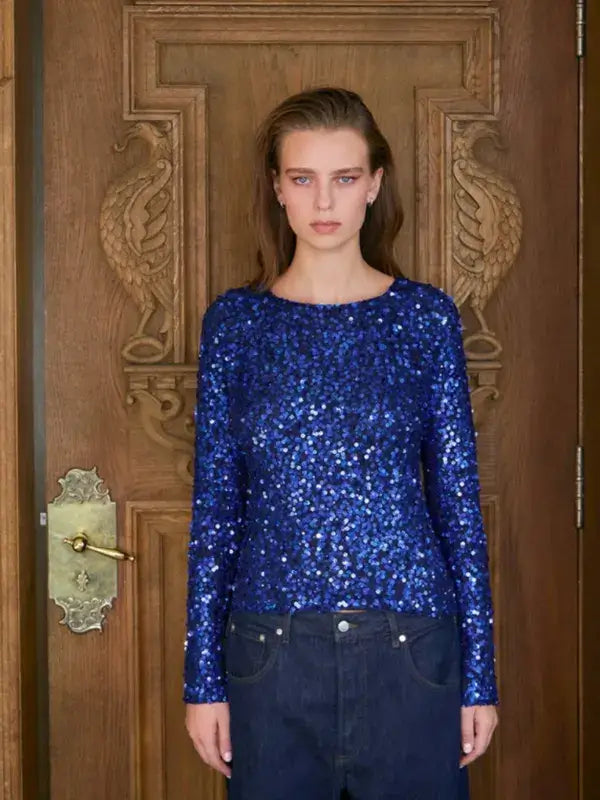 A person wearing a royal blue Sandnes Garn Isla Sweater – neulesetti Paljett with sequined yarn and dark blue jeans.