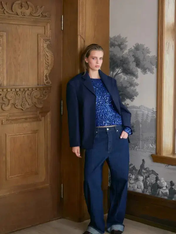 A person wearing a blue Sandnes Garn Isla Sweater – neulesetti Paljett under an oversized navy blazer and dark denim jeans.