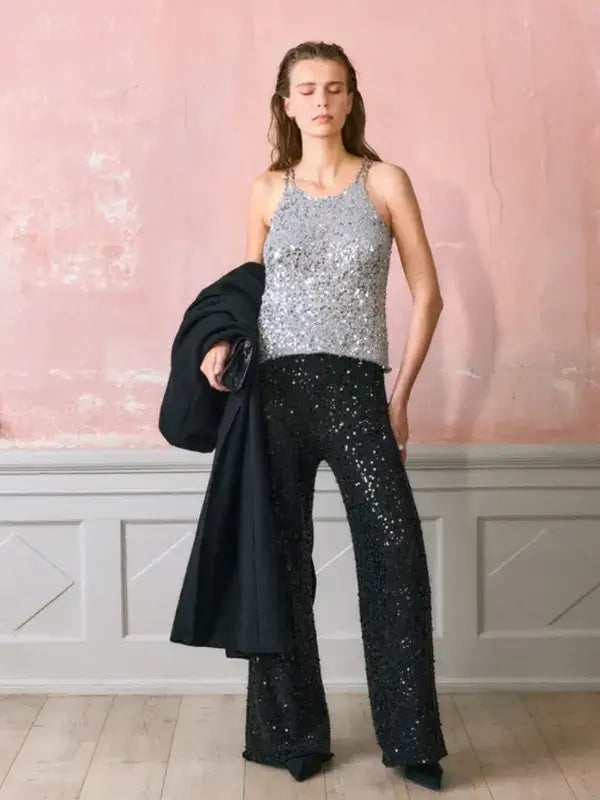 A woman in a Sandnes Garn Nia top – paljettitopin neulesetti and black sequined flared trousers, holding a black coat.