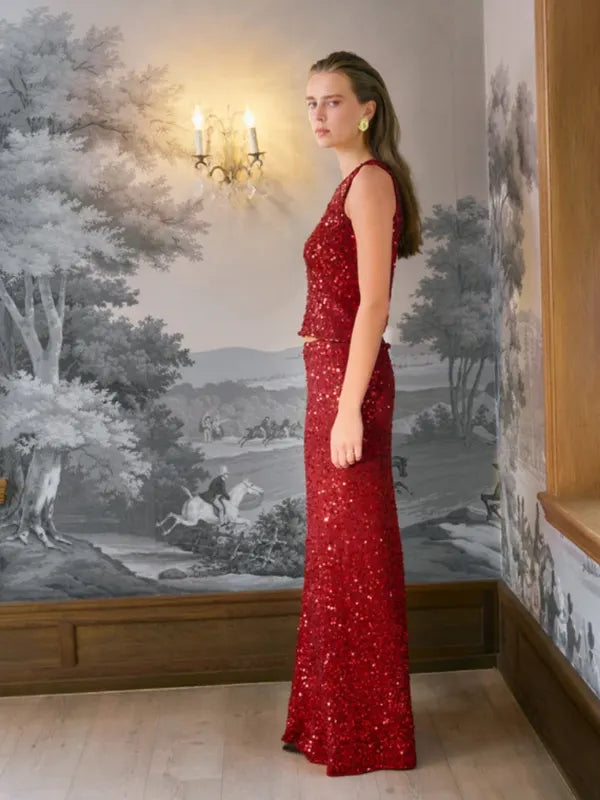 A woman wearing a sleeveless, red sequined Sandnes Garn Vale Top – neulesetti Paljett and a matching full-length skirt.