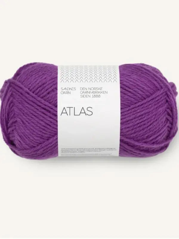 A skein of Sandnes Garn Atlas yarn in purple rests against a plain, light background. The label, showcasing a clean and modern design with Norwegian text, notes that the yarn is made from Norwegian lamb’s wool (norjalainen karitsanvilla) and merino wool (merinovillalanka).