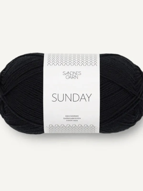 A skein of black Sandnes Garn Sunday fingering weight yarn with a white label featuring Norwegian text and a simple pattern; made from mulesing-free merino wool.