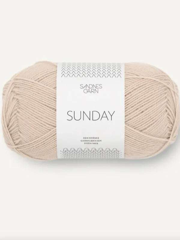 A beige ball of Sandnes Garn Sunday merinovillalanka with a minimalist white label displays the brand and product name. This mulesing-free yarn combines ethical production with stylish design.