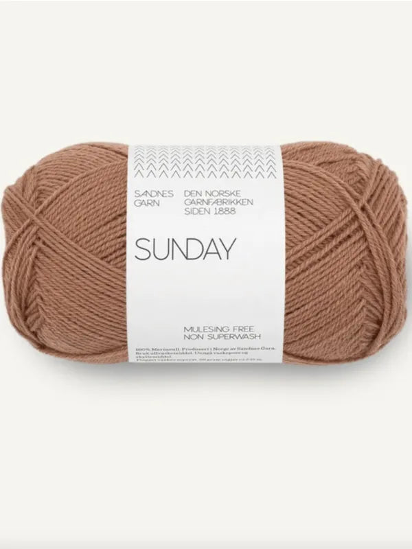A ball of light brown Sandnes Garn Sunday merino yarn with a white label displaying the brand, "mulesing-vapaa," and "Non Superwash," along with additional product details.