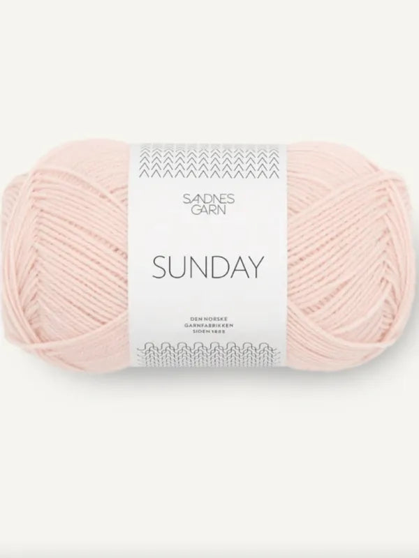 A skein of light pink Sandnes Garn Sunday merino wool yarn, labeled as mulesing-free, sits against a plain background. It features a minimalist white label with simple text and a decorative top pattern.