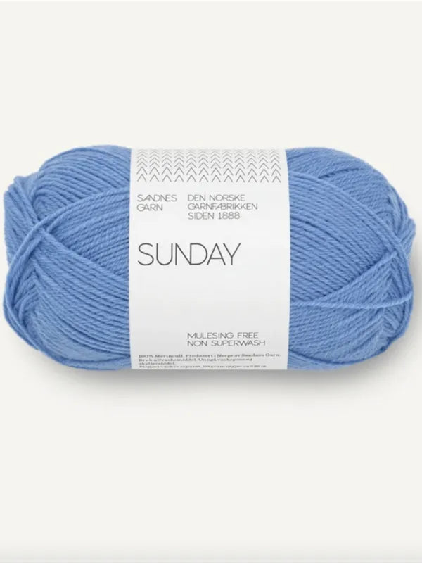 A skein of Sandnes Garn Sunday yarn in light blue, made from mulesing-free merino wool, wrapped with a white paper band displaying product info in English and Norwegian.