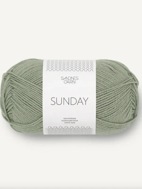 A light sage green ball of Sandnes Garn Sunday merino wool yarn, mulesing-free, wrapped in a white paper band with minimalist text and subtle decorative patterns.
